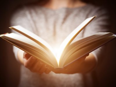 Light coming from book in woman's hands in gesture of giving, offering. Concept of wisdom, religion, reading, imagination.